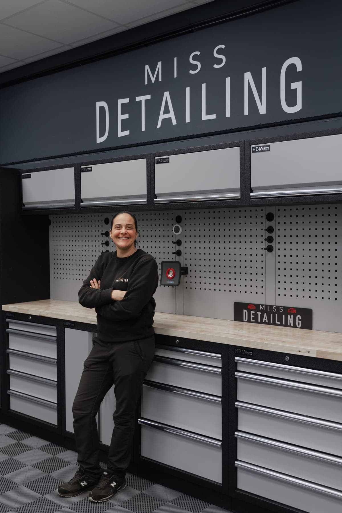 Portrait souriant dans l'atelier Miss Detailing, accoudée à l'établi devant le logo